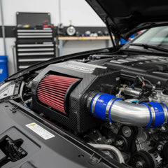 High-performance carbon fiber air intake system with blue silicone couplers installed in a car engine bay, featuring RawTorque automotive tuning parts.