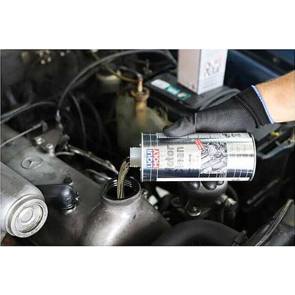 Person pouring a motorclean liquid from a can into a car engine, with a focus on the action of refilling or servicing.